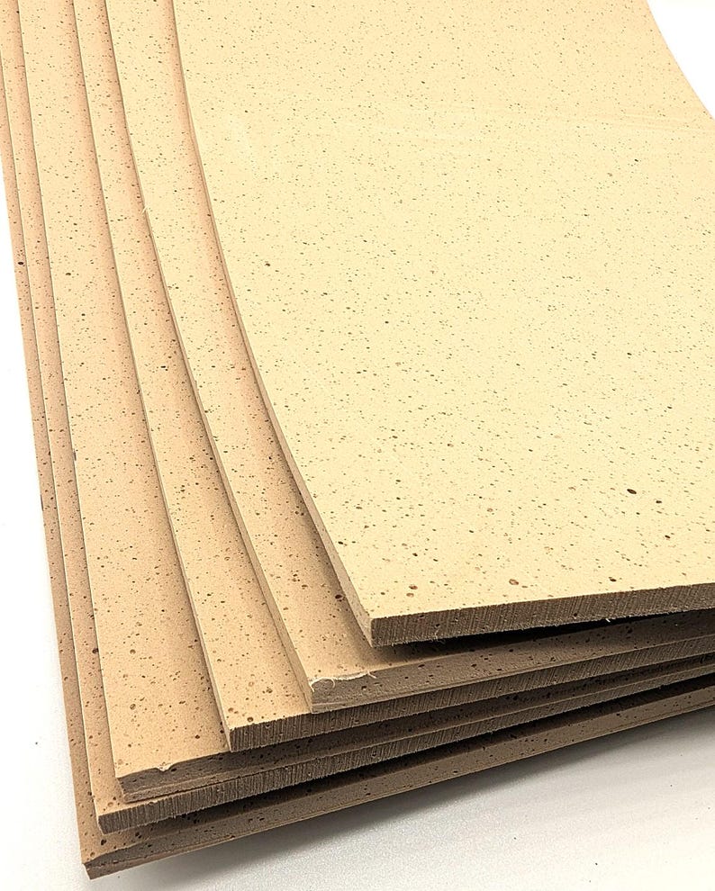May include: A stack of rectangular cork sheets. The sheets are a light tan colour with small, dark speckles throughout. The edges of the sheets are a darker brown, and the sheets are stacked on top of each other.
