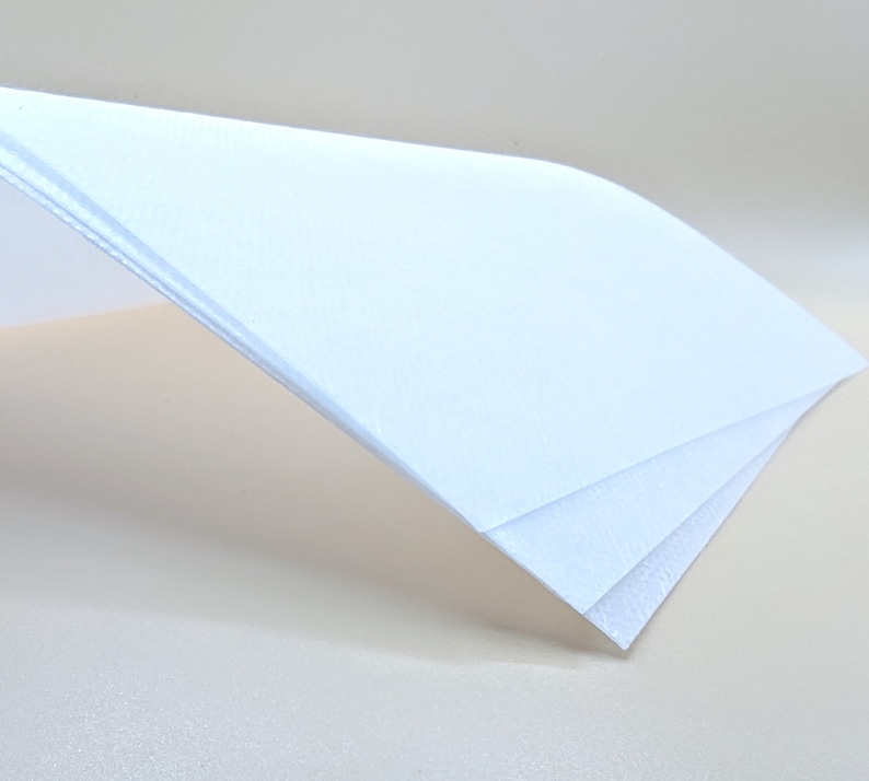 May include: Three sheets of white paper stacked on top of each other. The top sheet is folded over the other two sheets.