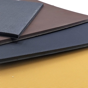 Pode incluir: Quatro tapetes de borracha de cores diferentes empilhados uns sobre os outros. O tapete superior é preto, o segundo é castanho, o terceiro é cinzento escuro e o tapete inferior é amarelo.