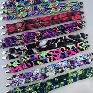 May include: A collection of adjustable fabric straps featuring various colorful patterns including neon swirls, animal prints, floral designs, and abstract shapes. Each strap is equipped with silver-toned metal clips and sliders for length adjustment.