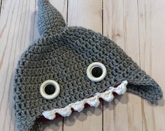 May include: Gray crocheted shark hat with white teeth and black button eyes.