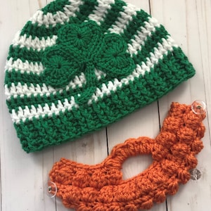 May include: A green and white crocheted hat with a shamrock design and an orange crocheted beard.