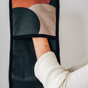May include: A black oven mitt with a geometric pattern of brown, beige, and black circles. The mitt is hanging on a white wall.