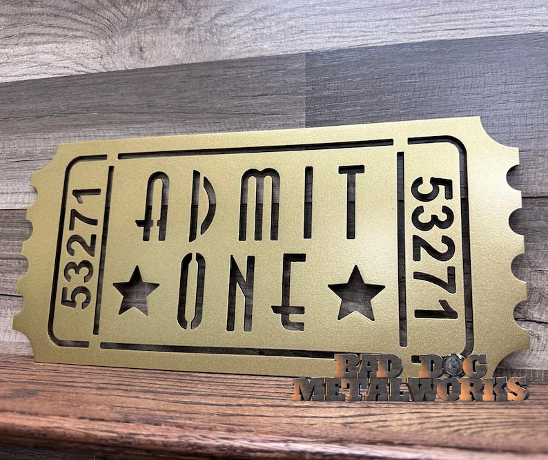 May include: Gold metal ticket-shaped sign with the text "ADMIT ONE" and the numbers "53271" on either side. Two stars are on either side of the word "ONE".