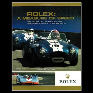 May include: An advertisement for Rolex featuring vintage race cars. The main image shows two blue and white race cars with drivers, one with the number 79 and the other with 98. Text reads "ROLEX: A MEASURE OF SPEED".