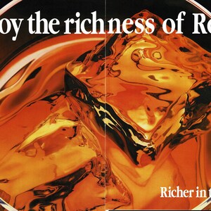 May include: Close-up of a glass filled with amber liquid and ice cubes. The text "Enjoy the richness of Red" is at the top, with "Richer in taste" at the bottom. The drink appears to be a whiskey or similar spirit.