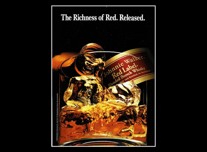 May include: An advertisement for Johnnie Walker Red Label blended Scotch whisky. The image features a glass filled with ice cubes and amber-colored liquid, with the brand's label visible. The text "The Richness of Red. Released." is at the top.