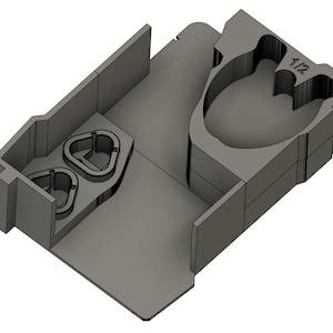 Pode incluir: Um organizador de plástico cinza, impresso em 3D, com vários compartimentos. Apresenta dois suportes triangulares e uma seção maior e arredondada com a etiqueta "1/2". O design sugere uma solução de armazenamento para itens pequenos.
