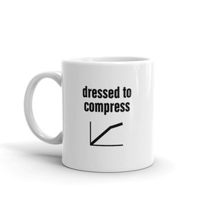 Może przedstawiać: Biały kubek ceramiczny z czarnym nadrukiem "dressed to compress" i wykresem liniowym ze wzrostową tendencją.