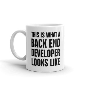 Pode incluir: Caneca de cerâmica branca com uma alça curva. A caneca apresenta o texto "THIS IS WHAT A BACK END DEVELOPER LOOKS LIKE" em letras pretas em negrito, um presente divertido para um desenvolvedor de software.