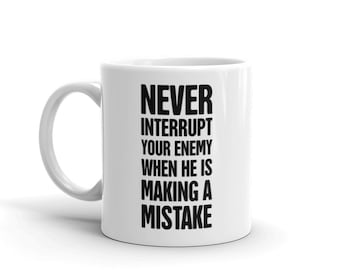 May include: White ceramic coffee mug with black text that reads "Never interrupt your enemy when he is making a mistake."