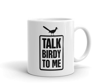 May include: White ceramic mug featuring a black silhouette of a roadrunner bird perched on a sign that reads "Talk Birdy To Me".
