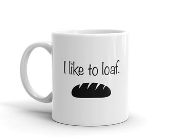 Könnte beinhalten: Weiße Keramik-Tasse mit dem schwarzen Schriftzug "I like to loaf" über einer schwarzen Brotlaib-Illustration. Die Tasse hat einen gebogenen Henkel und ist für heiße oder kalte Getränke geeignet.