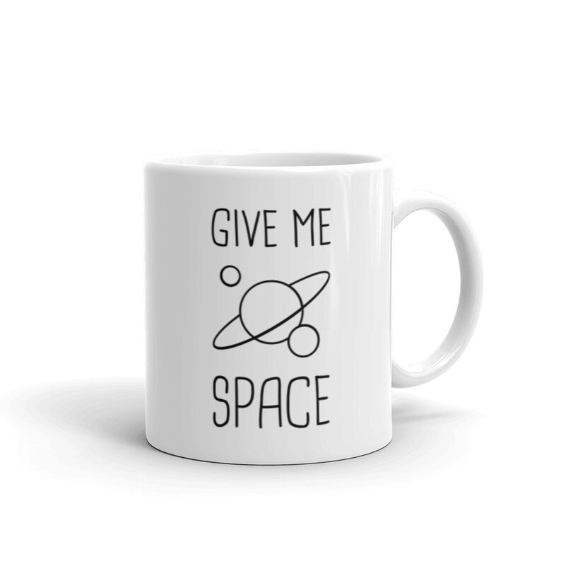 May include: White ceramic coffee mug with black text that reads "GIVE ME SPACE" and a simple line drawing of a planet with rings and a smaller moon.