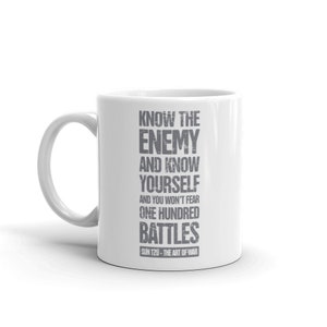 Op de afbeelding: Witte keramische mok met een gebogen handvat. De mok bevat de quote "KNOW THE ENEMY AND KNOW YOURSELF AND YOU WON'T FEAR ONE HUNDRED BATTLES" toegeschreven aan Sun Tzu uit The Art of War, in grijze tekst.