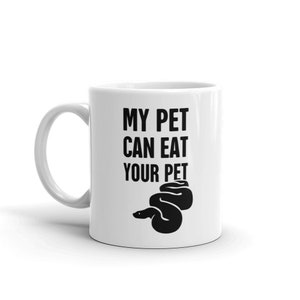 Könnte beinhalten: Weiße Keramik-Tasse mit dem schwarzen Text "MY PET CAN EAT YOUR PET" und einer schwarzen Schlange. Die Tasse hat einen gebogenen Henkel und eine zylindrische Form.