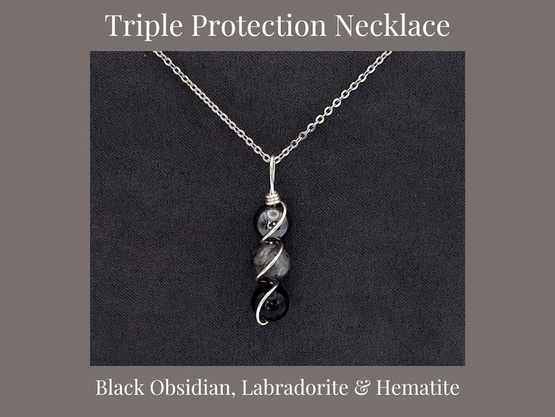 May include: A silver chain necklace with three gemstone beads: black obsidian, labradorite, and hematite. The beads are wrapped in silver wire. The text "Triple Protection Necklace" and "Black Obsidian, Labradorite & Hematite" are displayed.