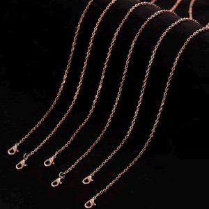 May include: Several rose gold-colored chain necklaces with lobster claw clasps are displayed against a dark background. The chains are thin and delicate, with a subtle shine, suggesting they are made of metal.