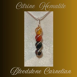 May include: A silver chain necklace with a pendant made of six round gemstone beads. The beads are in a gradient of colors, starting with a light yellow citrine bead, followed by a carnelian bead, a bloodstone bead, a black hematite bead, and ending with a dark green bead. The text "Citrine Hematite Bloodstone Carnelian" is written below the pendant.