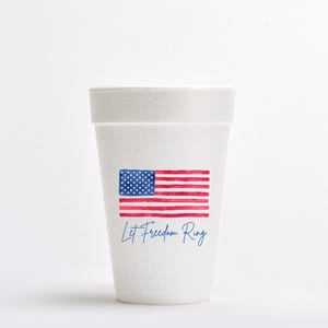 May include: White foam cup with a printed American flag design. The flag features red and white stripes with a blue square of stars. Below the flag, the text "Let Freedom Ring" is written in a blue script font.