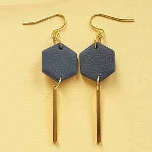 May include: A pair of dangle earrings with a dark gray hexagonal charm and a gold bar pendant.