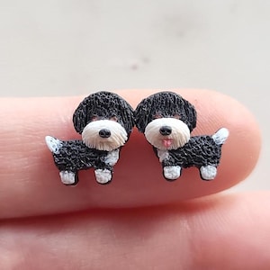 May include: A pair of black and white dog stud earrings. The dogs are facing forward with their tongues sticking out.
