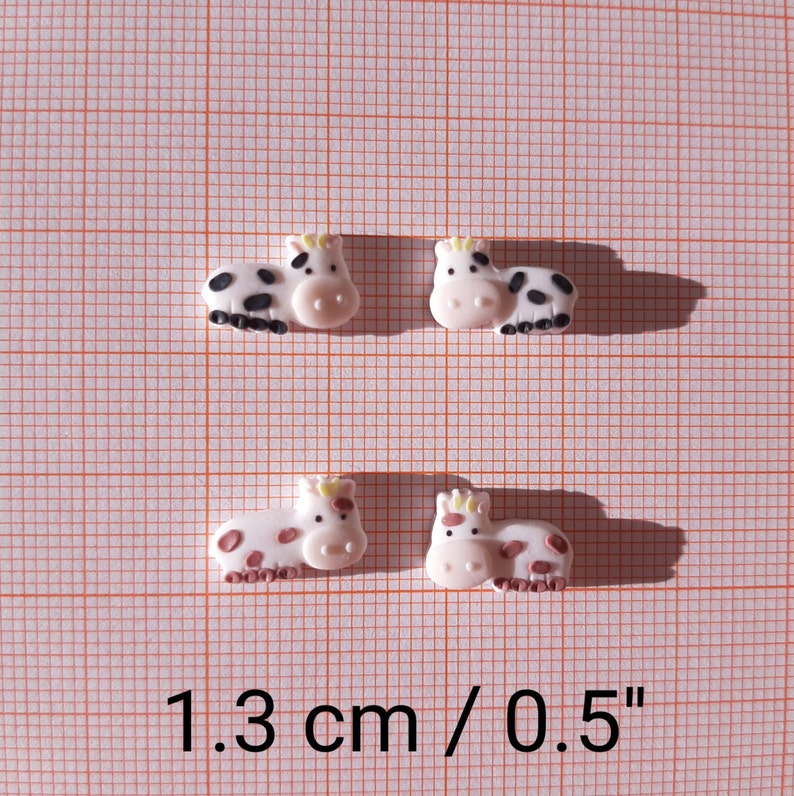 Pu&ograve; includere: Quattro figurine di mucca in ceramica bianca con macchie nere e marroni. Le figurine sono alte 1,3 cm.