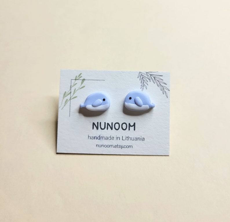 May include: A pair of light blue whale stud earrings on a white card with the text "NUNOOM handmade in Lithuania nunoom.etsy.com"