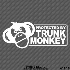 May include: White decal featuring a cartoon monkey face and the text "PROTECTED BY TRUNK MONKEY" in a rectangular frame. The decal is shown on a gray background. The text "WHITE DECAL" is at the bottom.