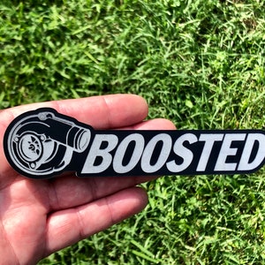 May include: A black and silver sticker with a turbocharger graphic and the word "BOOSTED" in white lettering.