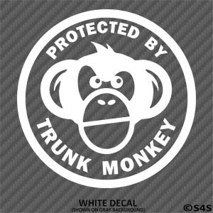 May include: White decal featuring a cartoon monkey face inside a circular frame. The text "PROTECTED BY TRUNK MONKEY" is arched around the monkey. The words "WHITE DECAL" are at the bottom.