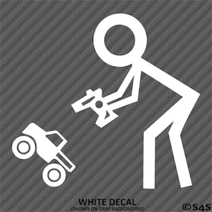 Może przedstawiać: Biała naklejka przedstawiająca ludzika trzymającego pilota i monster trucka. Tekst "WHITE DECAL (SHOWN ON GRAY BACKGROUND)" znajduje się na dole. Tło to szary, teksturowany wzór.