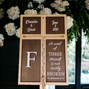 May include: A wooden sign with a brown background and white text. The sign reads "Chandler & Sarah, June 8, 2024". Below the date, it says "A cord of THREE strands is not easily BROKEN, Ecclesiastes 4:12".