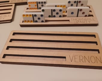 May include: Wooden domino rack with five slots for dominoes. The rack is labeled "Vernon".