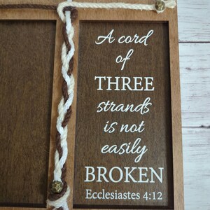 May include: Wooden framed sign with a dark brown finish, featuring the text "A cord of THREE strands is not easily BROKEN" in white. The sign includes a braided rope design and the text "Ecclesiastes 4:12".