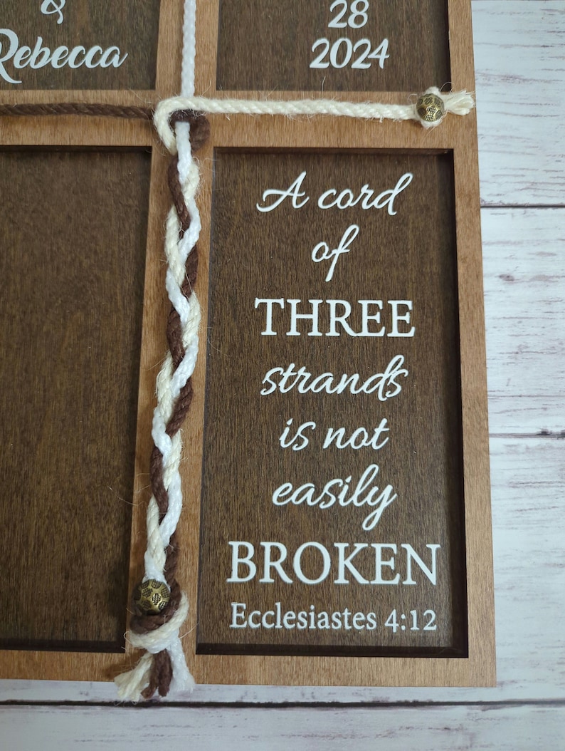 May include: Wooden framed sign with a dark brown finish, featuring the text "A cord of THREE strands is not easily BROKEN" in white. The sign includes a braided rope design and the text "Ecclesiastes 4:12".