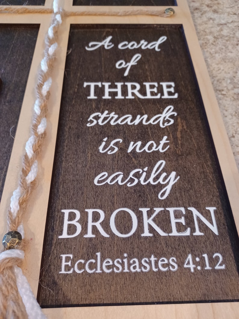 May include: Wooden framed sign with the text "A cord of three strands is not easily broken" from Ecclesiastes 4:12. The sign has a dark brown background with white lettering and a braided rope detail.