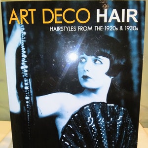 May include: Book cover featuring a black and white photo of a woman with short, dark hair, wearing a beaded necklace and holding a black fan. The title of the book is "Art Deco Hair" and the subtitle is "Hairstyles from the 1920s & 1930s". The book also states "Over 350 Illustrations & Diagrams!" and the author is "Daniela Turudich".