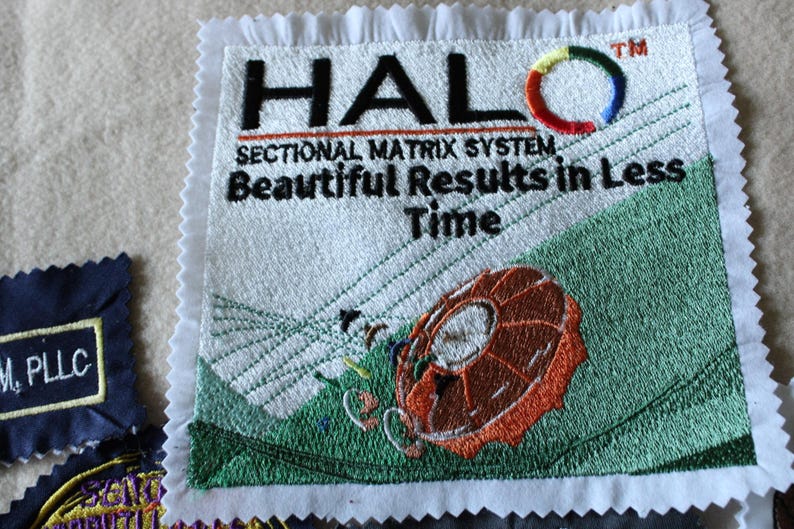 May include: Embroidered patch with the word "HALO" in black, a colorful circular design, and the text "SECTIONAL MATRIX SYSTEM Beautiful Results in Less Time." The patch features a brown and orange design on a green background.