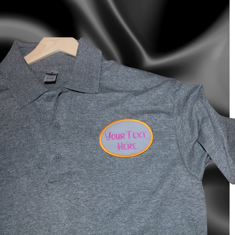 May include: Gray polo shirt with a gray oval patch that says "YOUR TEXT HERE" in pink lettering with an orange outline.