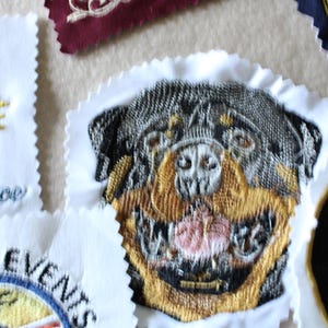 May include: Embroidered patches with various designs, including a Rottweiler dog, a tree, and text. The patches feature detailed stitching in multiple colors, with a white scalloped edge. The patches are likely for clothing or accessories.