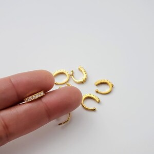 Puede incluir: Un conjunto de aros para la nariz de color dorado con brillantes transparentes. Los aros tienen forma de semic&iacute;rculo y tienen un peque&ntilde;o espacio para una f&aacute;cil inserci&oacute;n.