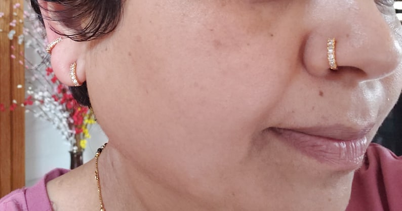 Puede incluir: Una mujer con pendientes de aro de oro con peque&ntilde;as piedras transparentes y un aro de nariz de oro con piedras transparentes.