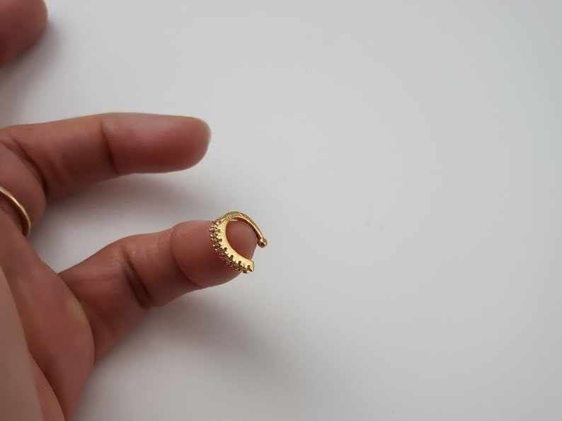 Puede incluir: Un aro para la oreja de color dorado con una fila de peque&ntilde;os diamantes de imitaci&oacute;n transparentes alrededor del borde.