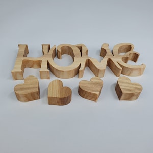 May include: Wooden "HOME" sign with individual letters and four wooden heart shapes. The letters and hearts are made of light-colored wood, with visible grain patterns. A decorative item for home decor.