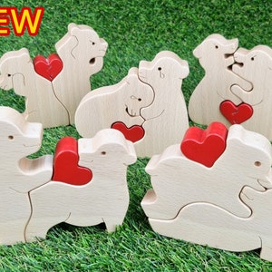 May include: Wooden bear and sheep puzzles with red heart accents. The puzzles are light brown and interlock to form pairs. The word "NEW" is in a red box in the upper left corner. The puzzles are on a green surface.