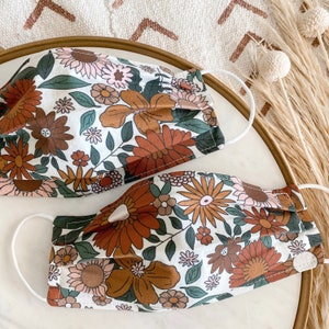 Peut inclure: Deux masques en tissu blanc avec un motif floral brun et blanc. Les masques sont pliss&eacute;s et en coton.