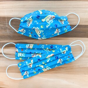 May include: Two blue face masks with white elastic ear loops. The masks feature a repeating pattern of R2-D2 robots and other Star Wars characters on a blue background.