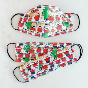 May include: Three white face masks with a colorful pattern of cartoon characters singing Christmas carols. The characters are from the Peanuts comic strip.
