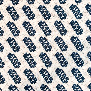 May include: White fabric with a repeating pattern of the words "Star Wars" in black text. The background is a light beige with small black and orange dots.